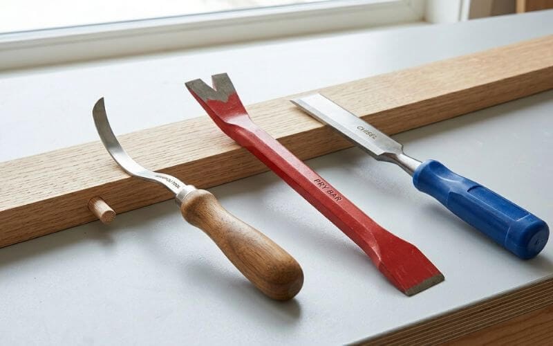 A visual comparison of the Levapioli tool, a red pry bar, and a blue-handled chisel on a workbench, showing their different prying and lifting edges.