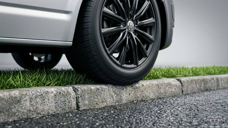A professional macro photograph showing a car tire touching a pavement curb to demonstrate the strict Falkirk pavement parking ban.